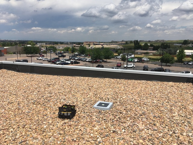 A Hailios Tessera sensor on a flat gravel-ballast rooftop, the dealership's vehicle lot spread out below