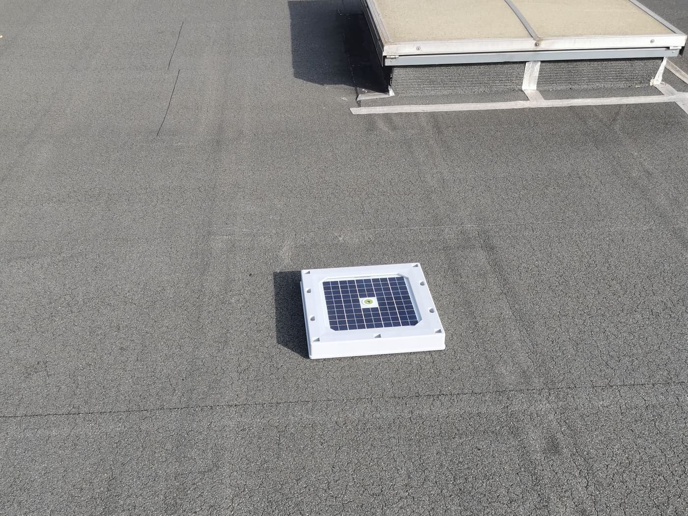 A Hailios Tessera sensor on a flat commercial roof membrane, a rooftop skylight just behind it