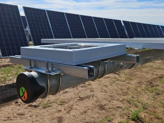 A Tessera sensor bracketed to the torque tube of a utility-scale solar tracker, rows of photovoltaic panels behind it under a blue sky